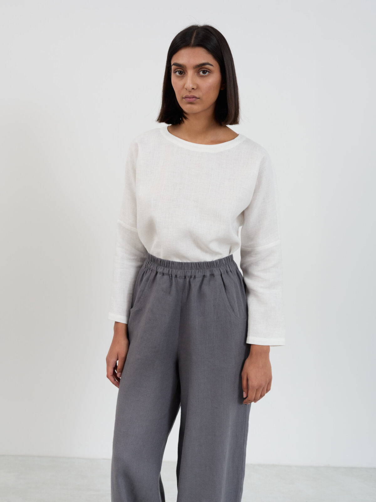 Front view of Haven charcoal linen barrel leg pants with elasticated high waist and relaxed fit through the hips, paired with a white linen top