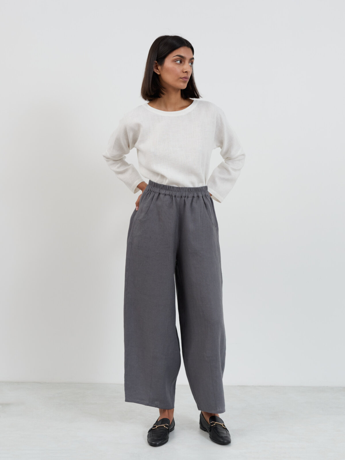Full front view of Haven linen pants in charcoal with hands in front side-seam pockets, showing the barrel leg shape and pull-on elastic waistband