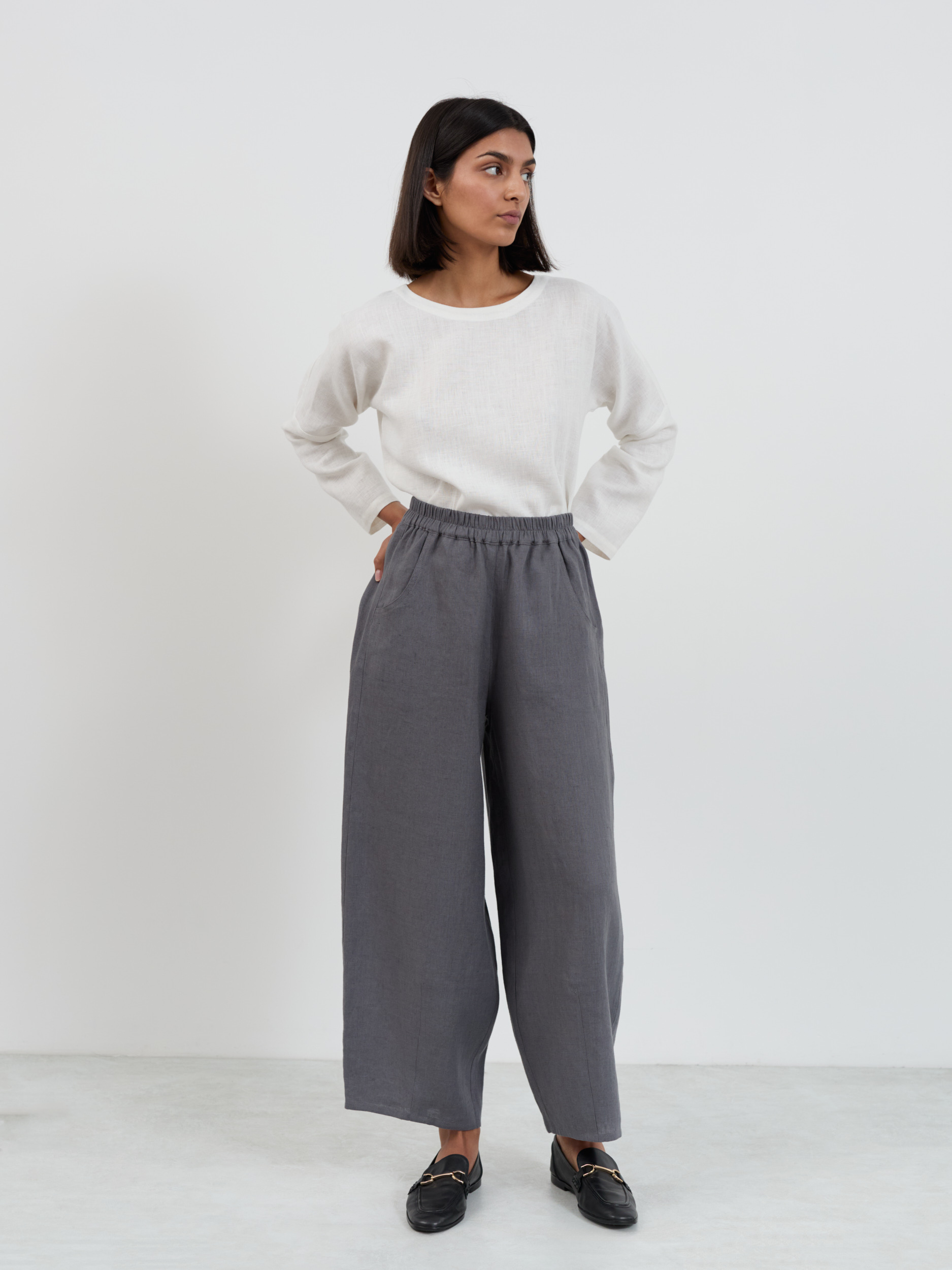 Full front view of Haven linen pants in charcoal with hands in front side-seam pockets, showing the barrel leg shape and pull-on elastic waistband