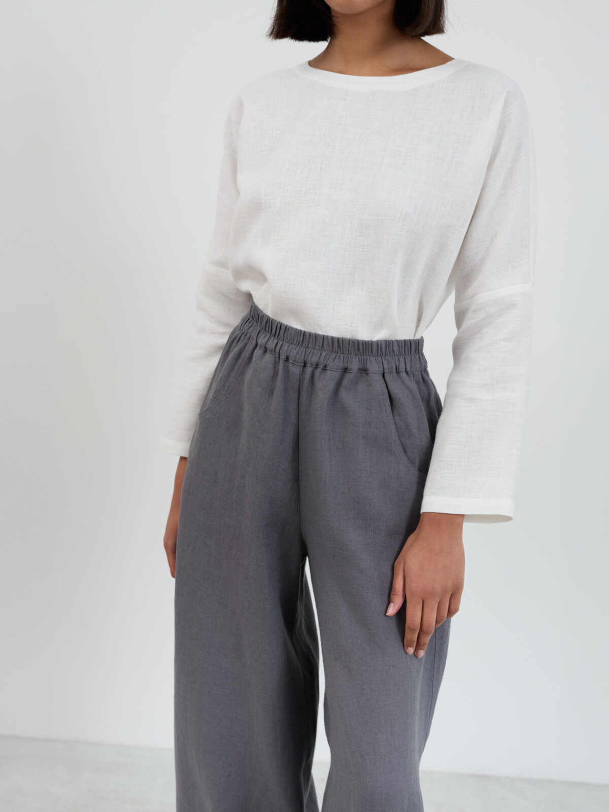 Close-up of Haven linen pants waistband and upper body showing gathered elastic detail, front side-seam pocket entry, and midweight linen texture in charcoal