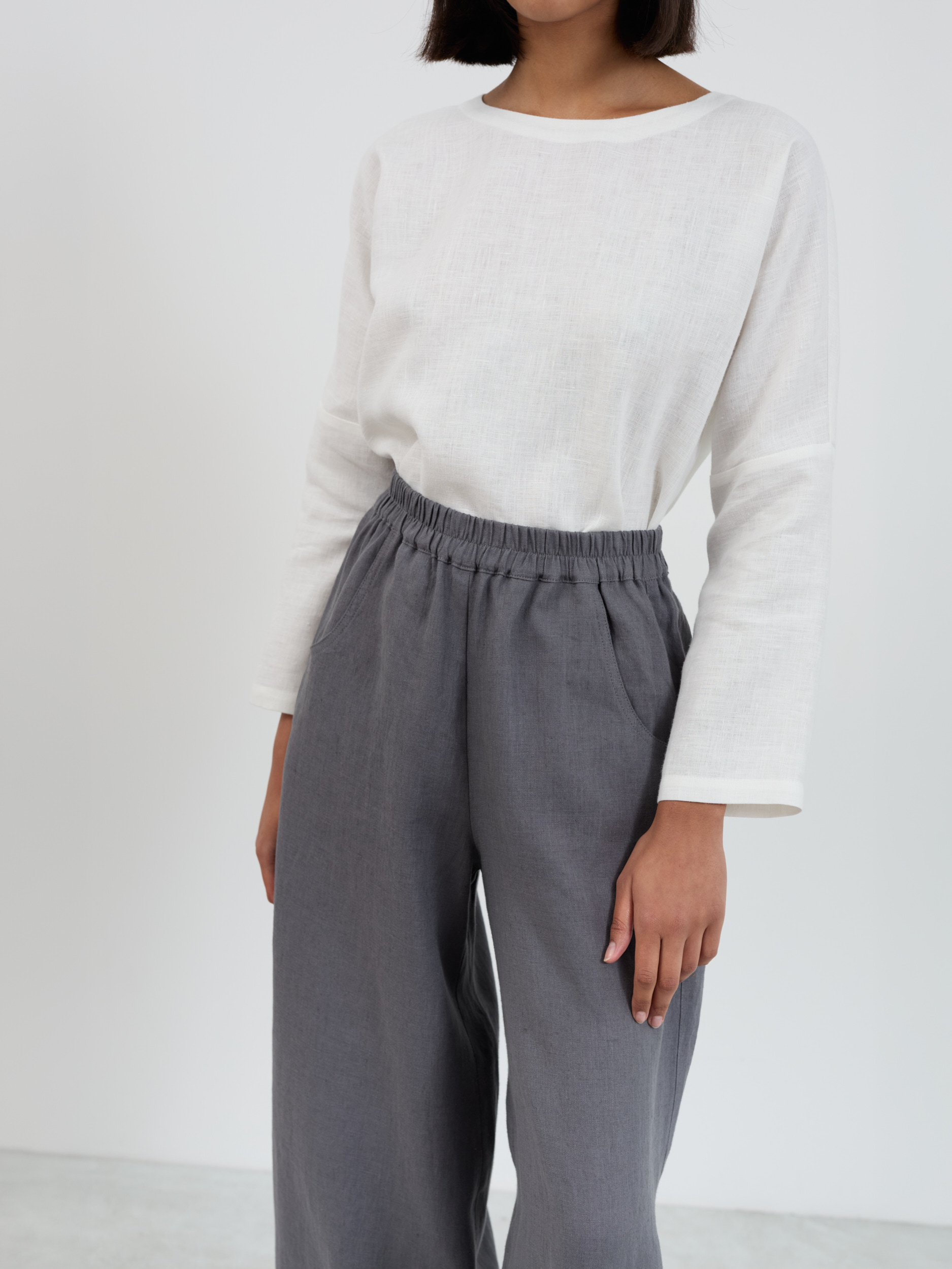 Close-up of Haven linen pants waistband and upper body showing gathered elastic detail, front side-seam pocket entry, and midweight linen texture in charcoal