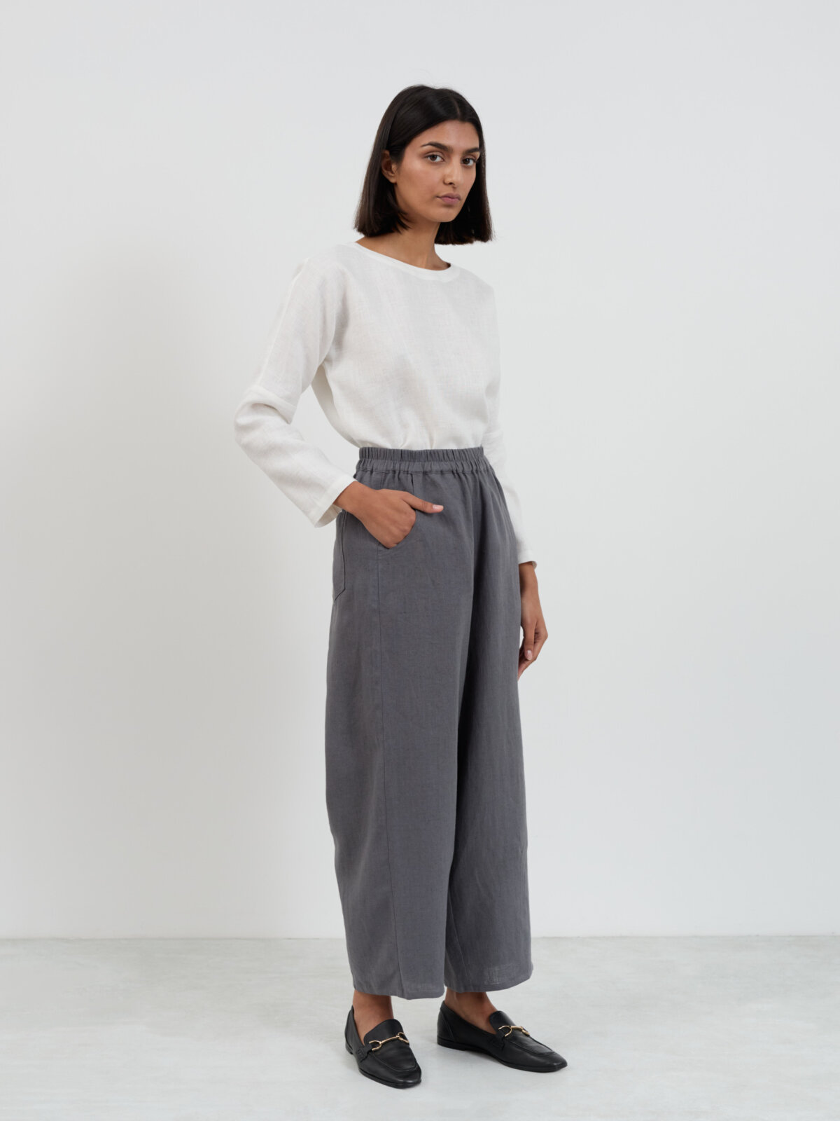 Three-quarter front view of Haven barrel leg linen pants in charcoal with hand in pocket, showing the wide leg silhouette from hip to ankle