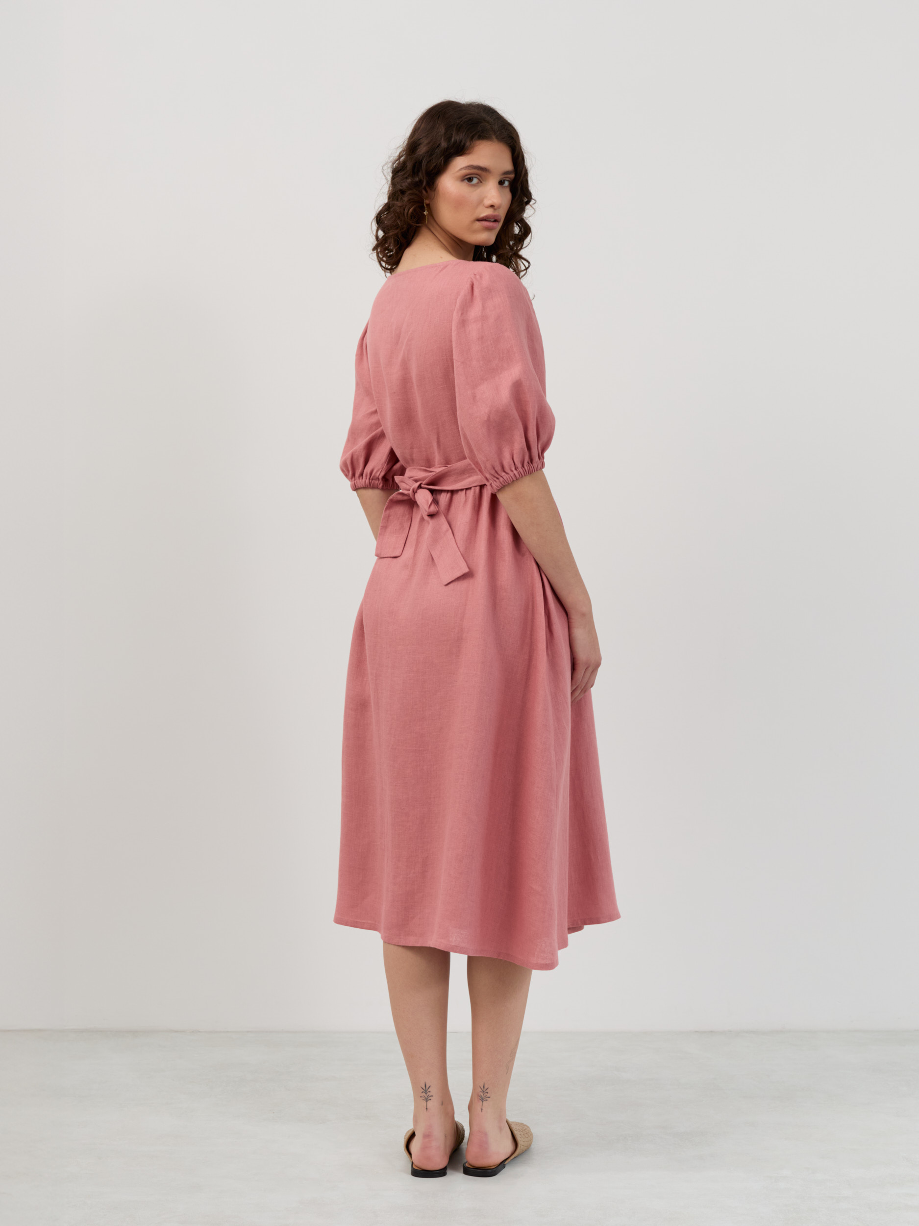Back view of salmon pink linen wrap dress showing self-fabric bow closure, puff sleeves and midi length
