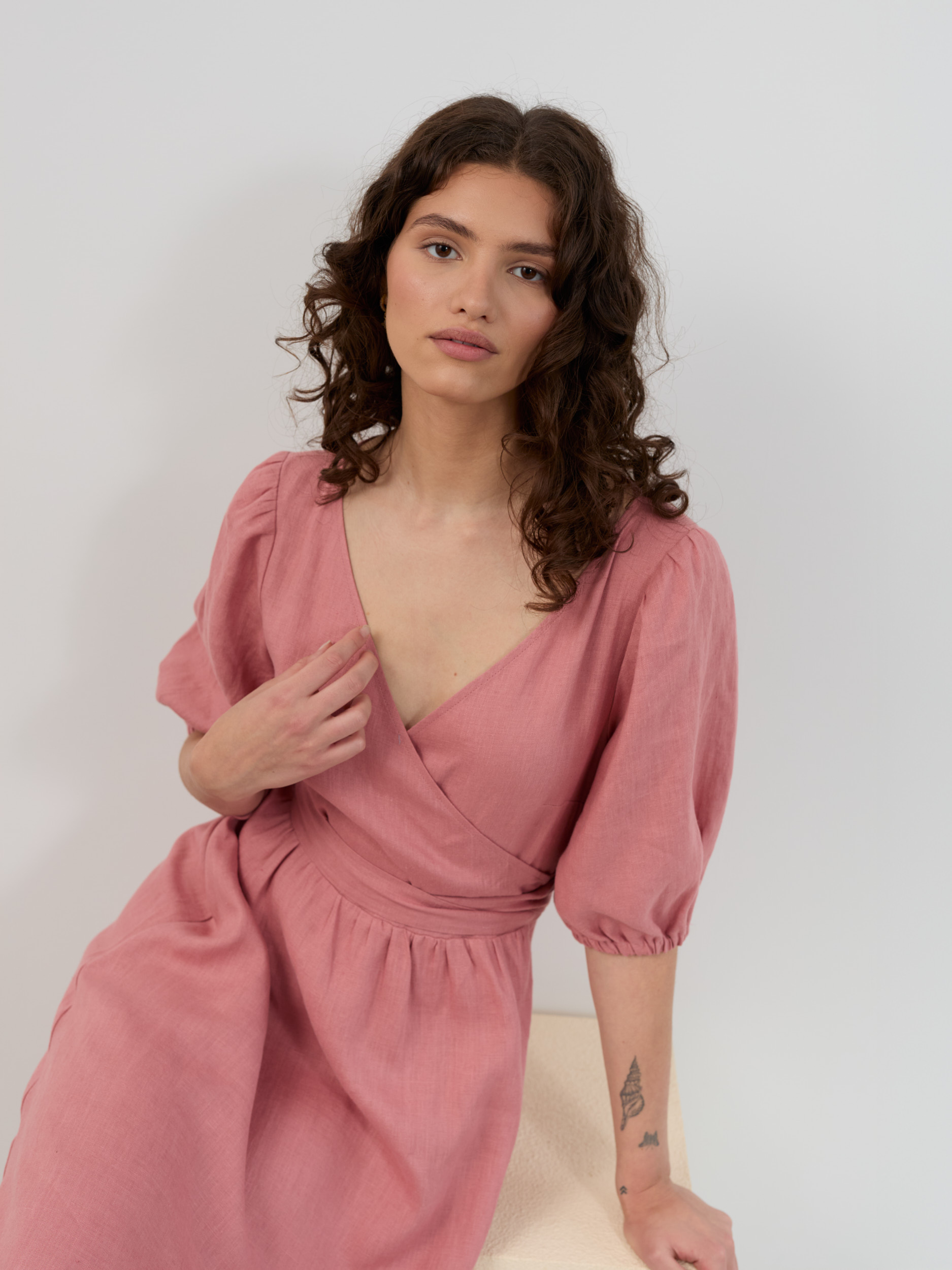 Seated close-up of salmon pink linen wrap dress showing V-neck bodice, puff sleeves and natural linen texture