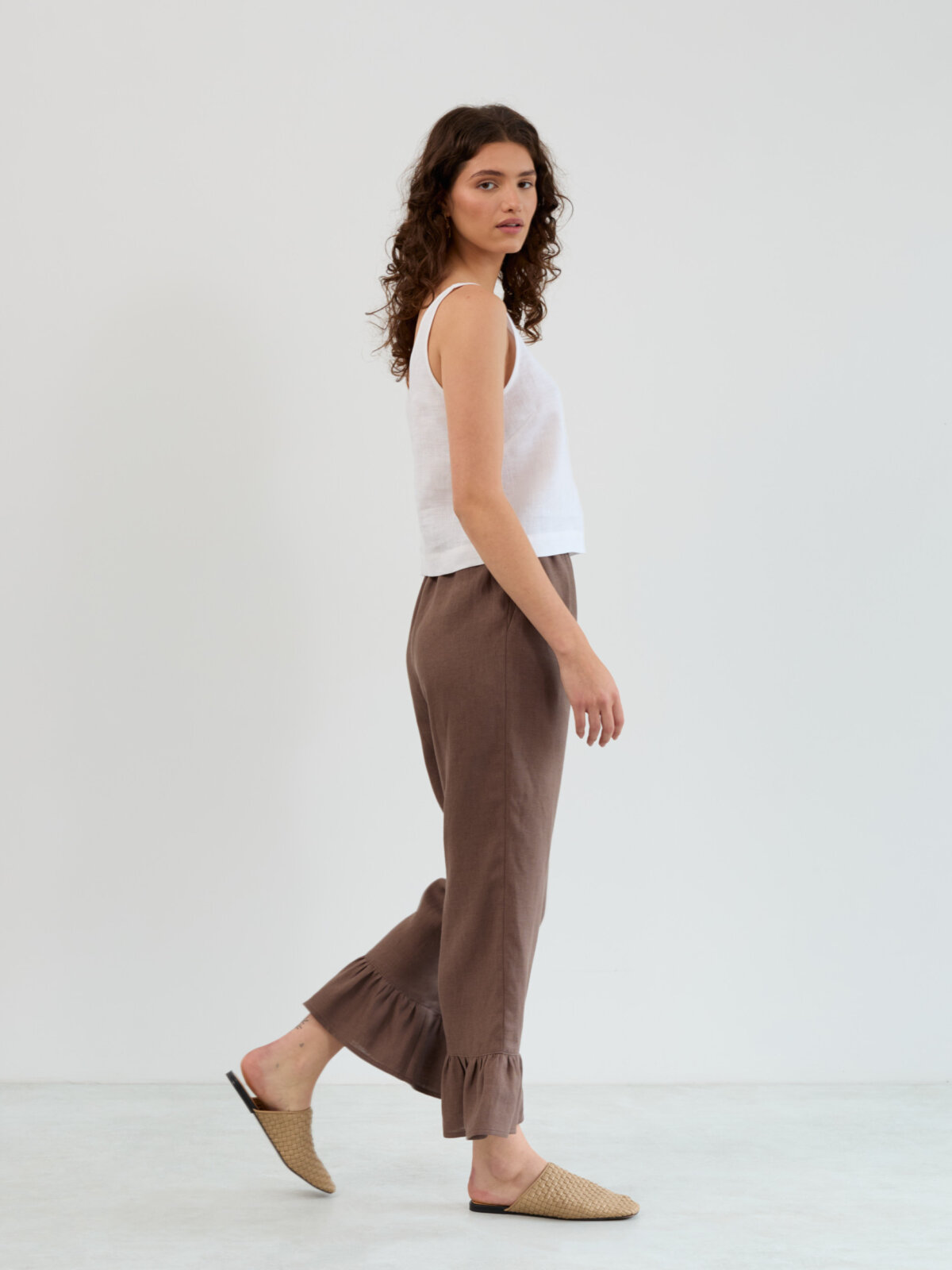 Side walking view of the Gigi linen ruffle pants in cocoa showing the straight leg and gathered flounce at the ankle